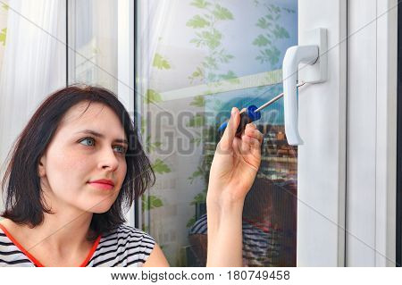 A young woman of 20 years old uninstalls the handle on the double-glazed window frame using a screwdriver.