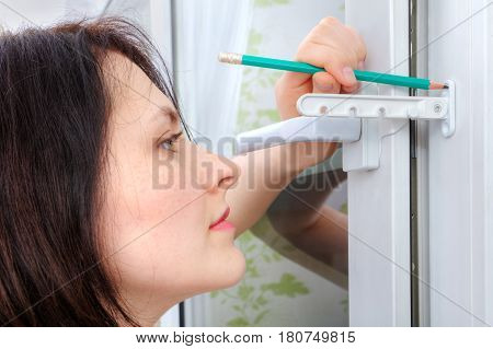 A young woman makes a marking for fixing the limiter on a plastic window.