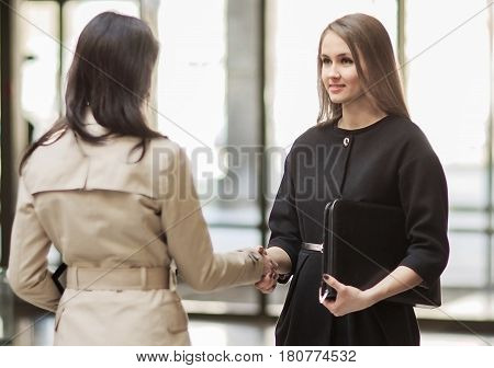 Two Businesswomen Shaking Hands In Modern Office
