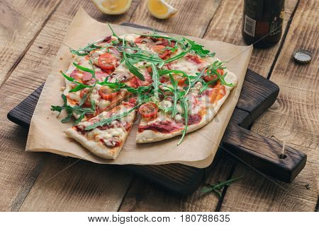 Italian pizza with salami cherry tomato mushrooms and arugula on wooden board with beer close up