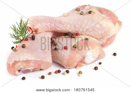 Three raw chicken drumsticks with a sprig of dill and peppercorns isolated on white background.