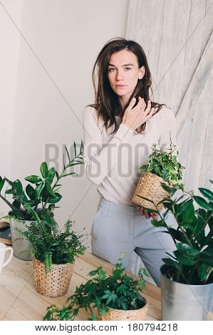 young woman watering flowerpots at home. Casual lifestyle series in modern scandinavian interior
