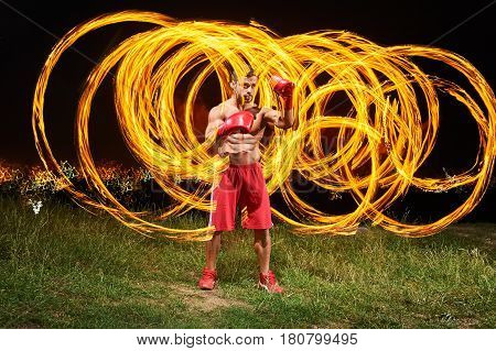 Shot of a young shirtless male fighter with strong fit and toned muscular body training outdoors at night fire and flames on the background copyspace burning fiery flame hot masculinity courage fight.