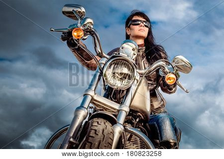 Biker girl in a leather jacket on a motorcycle looking at the sunset.