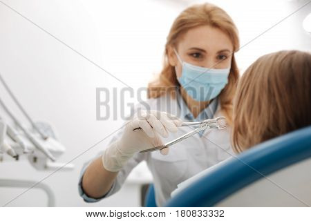I will make it quick. Young prominent specialist using a tool for extracting her patients baby tooth while wearing special uniform