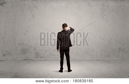 A confused sales person having a dilemma, standing with his back in empty grey urban environment concept