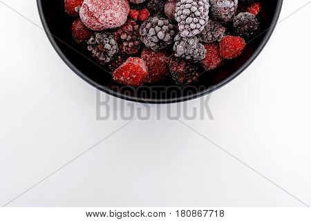 Frozen Berries in black bowl on white surface