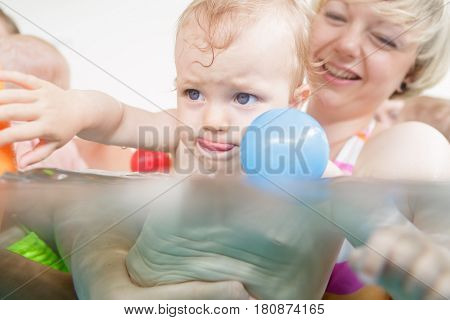 Mothers and their kids having fun at baby swimming lesson between lots of water balls