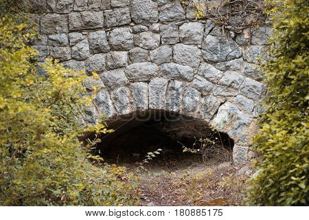 An old stone wall with an arch at the bottom among thickets.