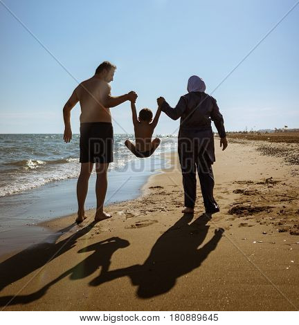 Muslim family, dad and mom with burkini on the beach walking near sea