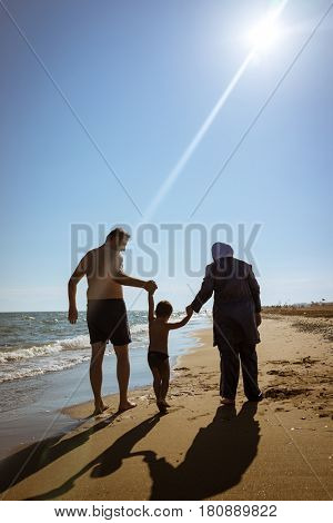 Muslim family, dad and mom with burkini on the beach walking near sea