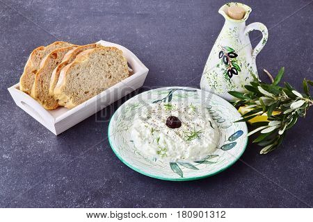 Greek traditional sauce tzatziki with olives, olive oil jar, lemon and bread on a grey abstract background. Healthy eating concept