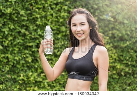 Asian woman in sportswear holding bottle of water on natural background. freshness happiness relaxing and smiling.