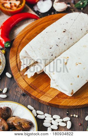 Vegetarian Burrito On Wooden Board Over Black Table Surrounded By Ingredients.
