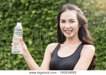 Asian woman in sportswear holding bottle of water on natural background. freshness happiness relaxing and smiling.