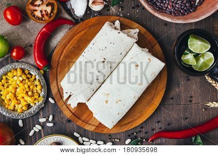 Vegetarian Burrito On Wooden Board Over Black Table Surrounded By Ingredients.