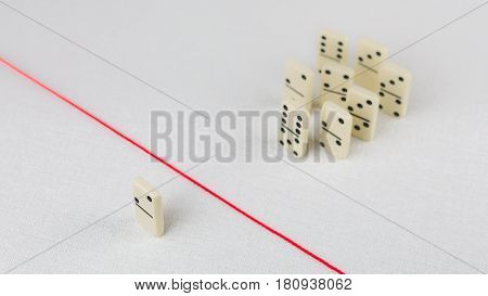 Expelled from the group, unable to cross the red line that separates them. Scene with group of domino. Concept of accusation guilty person, bulling or outcast in the team. Bright background.