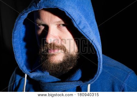 Solid bearded middle-aged man in a hood  portrait on black background