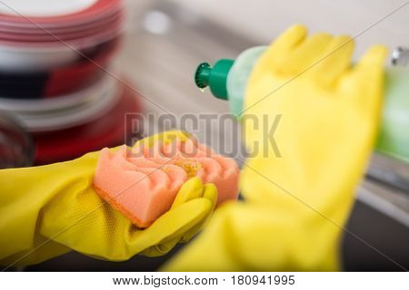 Cleaning dishware kitchen sink sponge washing dish. Close up of female hands in yellow protective rubber gloves washing