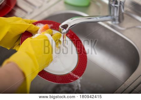 Cleaning dishware kitchen sink sponge washing dish. Close up of female hands in yellow protective rubber gloves washing