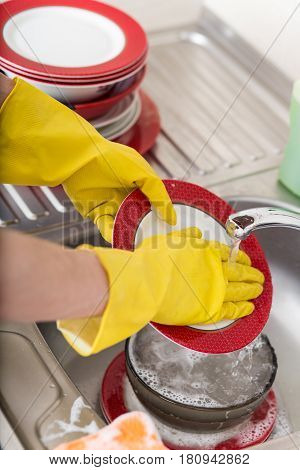 Cleaning dishware kitchen sink sponge washing dish. Close up of female hands in yellow protective rubber gloves washing