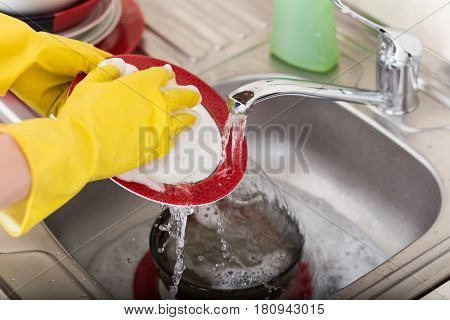 Cleaning dishware kitchen sink sponge washing dish. Close up of female hands in yellow protective rubber gloves washing