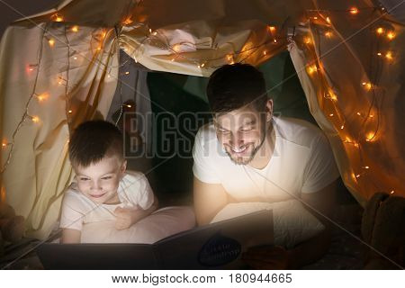 Father and son reading book in hovel at home