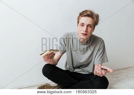 Incomprehensible man in jeans and t-shirt sitting on the floor and holding notebook in the hand while looking at the camera