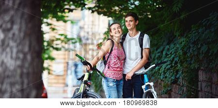 Young people, couple with bicycles in the park. A loving couple on a date on a summer evening. The guy with the girl hugs and kisses. Youth, first feelings, first love, first dates