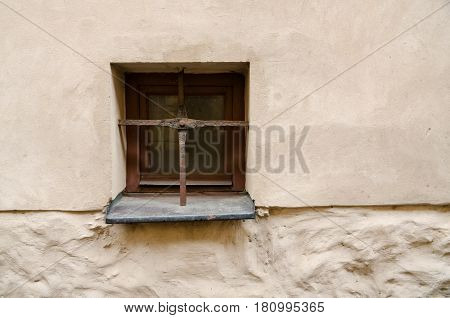A small window with an old grating in the wall. The grate is made in the form of two crossed steel bars.