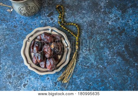 Dried Date Fruits Or Kurma Served On A Old Vintage Palte With Ornaments And Beads On A Blue Stone Ba