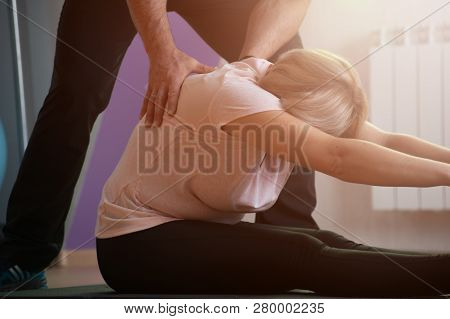 Close-up Aged Woman Engaged In Stretching Ligaments Under The Guidance Of A Male Trainer In The Gym.
