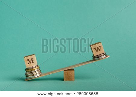 Gender Pay Gap. Wooden Cubes With M And W Letters On Seesaw With Different Stacks Of Coins, Men Get 