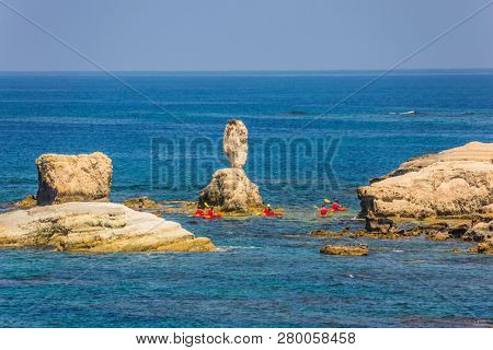 Picturesque coastline. Island of Cyprus in the Mediterranean Sea. Group of oarsmen on the red canoe. Concept of active and ecological tourism
