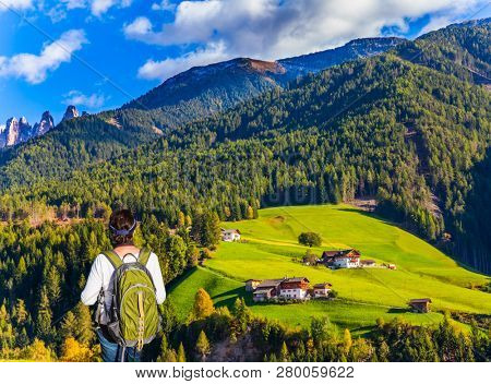 Middle-aged woman with a large green tourist backpack admires valley in the Dolomites. Wonderful day in South Tyrol. The concept of ecological and photo tourism. 
