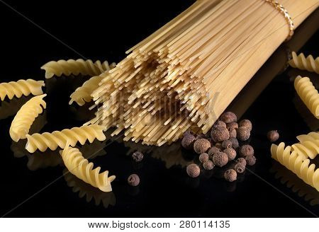 Italian Spaghetti, Isolated Against The Black Background. Yellow Italian Pasta, Black Pepper.