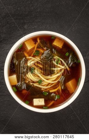 An Overhead Photo Of A Bowl Of Miso Shiru Soup With Tofu, Scallions, Noodles, And Wakame Seaweed On 