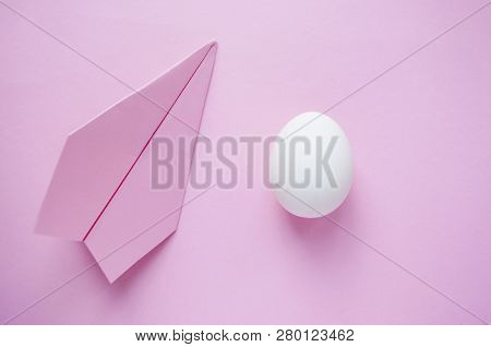A White Single Egg On Pink Background With Paper Plane And Copyspace. Travel Concept.