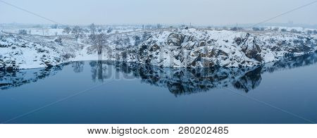 Blue Mirror Surface Of The River With A Reflection Of The Snow-covered Rocky Shore.