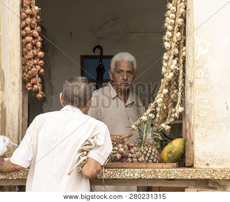 Trinidad, Cuba, Nov 27, 2017 - Store Keeper Specializing In Garlic Talks To Customer In Window