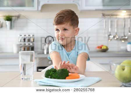 Adorable Little Boy Refusing To Eat Vegetables At Table In Kitchen