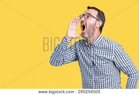 Handsome middle age elegant senior business man wearing glasses over isolated background shouting and screaming loud to side with hand on mouth. Communication concept.