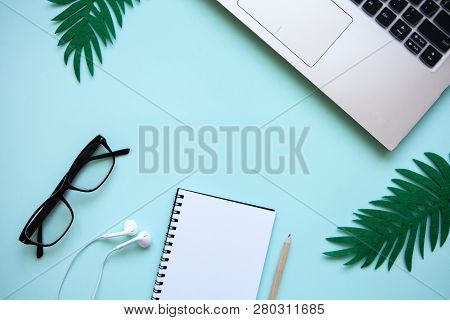 Workspace In A Trendy Blue Color. Many Different Items Including A Laptop, Glasses, Notebook, And He