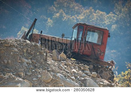 Old Red Tractor On A Stone Mound On A Background Of Trees