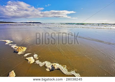 Breda sandstranden och havet skum på sand under utflöde