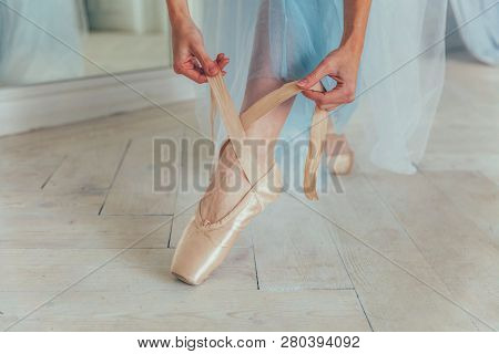 Hands Of Ballerina In Blue Tutu Skirt Puts On Pointe Shoes On Leg In White Light Hall. Young Classic