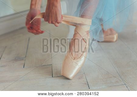 Hands Of Ballerina In Blue Tutu Skirt Puts On Pointe Shoes On Leg In White Light Hall. Young Classic
