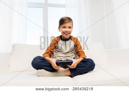 gaming, technology and people concept - smiling boy with gamepad playing video game at home