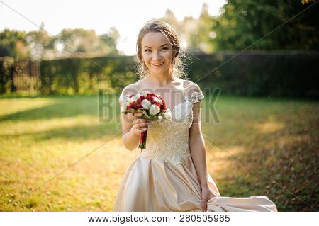 Smiling Bride In A White Wedding Dress Holding A Beauriful Red Roses Bouquet