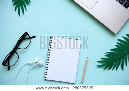 Workspace In A Trendy Blue Color. Many Different Items Including A Laptop, Glasses, Notebook, And He